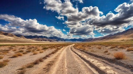Fototapeta premium The Dusty Dirt Track Road. Highway in to the mountains, with blue skies and clouds. Ideal Desktop background or Wallpaper.
