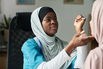 Muslim female doctor examining patient with stethoscope in a modern medical office. She is smiling...