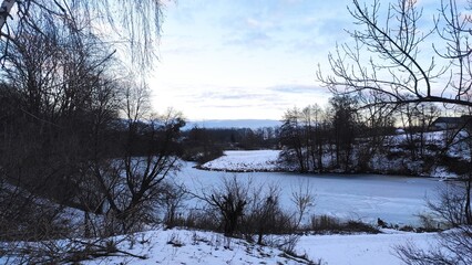 Winter landscape with a frozen river surrounded by snow-covered trees at dusk in a tranquil natural...