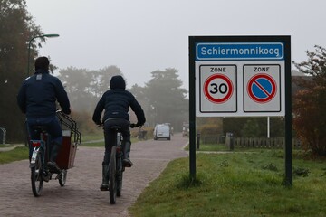 Two people are cycling near a place name sign (Schiermonnikoog in the Netherlands)