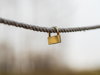 Locked  brass padlock hanging on a rope. Close-up