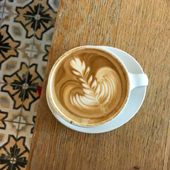 cup of coffee on wooden table with tile floor latte art white cup and saucer