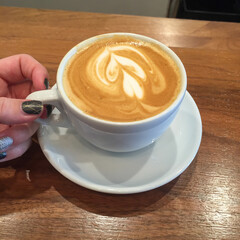 hand holding cup of coffee on wood table white mug and saucer latte art