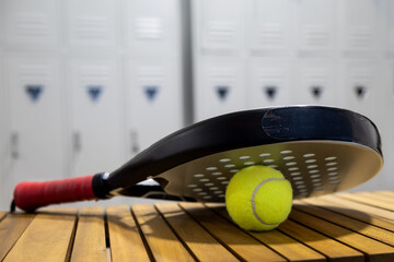 Padel tennis racket and ball resting on wooden bench near lockers in a sports facility