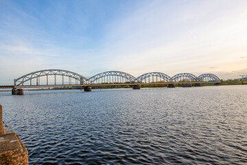 A modern electric passenger train crosses the railway bridge (Dzelzcea tilts) over the Daugava River. Taking passengers to the scenic Jurmala region of Latvia.