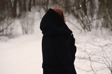 A red-haired girl in a black hood is standing with her back to him. Gothic winter atmosphere.