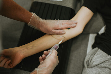 a nurse in gloves takes blood from a vein for analysis using a needle and a vacutainer