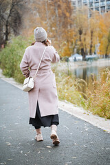 Fototapeta premium A woman dressed in a stylish pink coat and a matching hat is leisurely walking down a wellmarked path surrounded by various plants and trees, enjoying her stroll in the fresh air