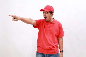 Angry Delivery employee asian man with red cap blank t-shirt uniform work courier service standing while pointing sideways. isolated on white background