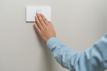 Asian young woman hand turn off on lighting switch at home room. Finger pushing light switch turn on or off white switch on wall for saving, control power electrical energy, eco environment concept.