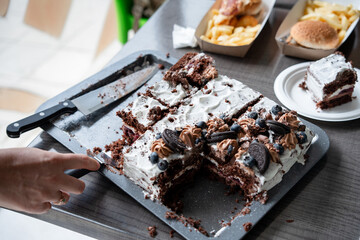 Hand slices a homemade chocolate cake into pieces, ready to be served to guests. Birthday or anniversary celebration. Party with non-diet treat brings people together to share in the sweetness. 