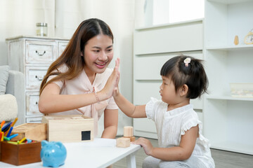 Asian female teacher high-fiving young girl during educational activity with blocks, celebrating achievement and building a supportive bond, fostering confidence and joy in nurturing home environment