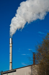 A single chimney with white smoke rising into the blue sky.