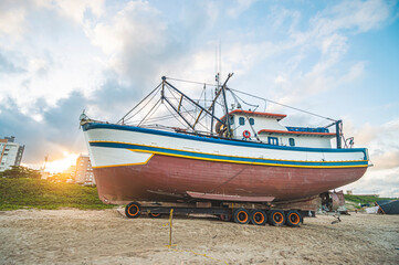 This photograph, taken on October 25, 2024, showcases a boat anchored in the sand of Navegantes, SC, Brazil, during a serene late afternoon. The setting sun