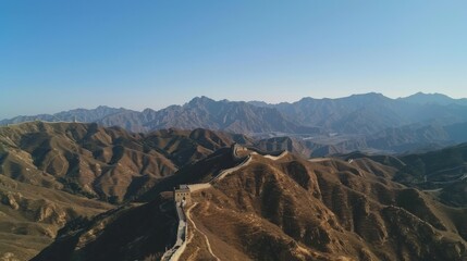 Obraz premium A sweeping view of the Great Wall of China snaking over the rugged mountains with a clear blue sky above, historic setting with rich earth tones, Wall style