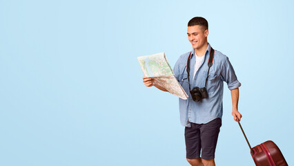 Lost in city. Young male tourist with suitcase holding city map, going towards copy space, orange studio background, panorama