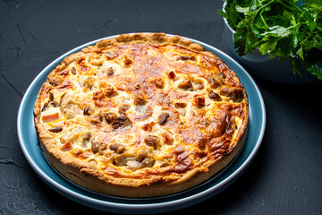 Quiche Laurent according to a traditional French recipe. Pie with chicken and mushrooms on a blue plate with a sprig of parsley on a black background. Close-up. Top view