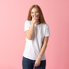 Lifestyles concept. A cheerful young woman in a white t-shirt covering her laugh with her hand