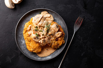 Fried chicken breast fillet in creamy mushroom sauce with champignons and oregano on the dark background top view