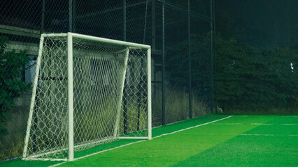 A soccer field at night with a goal in the center, illuminated by lamp posts