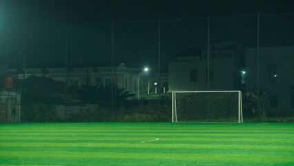 A soccer field at night with a goal in the center, illuminated by lamp posts