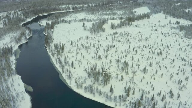 Discover the breathtaking landscape of northern Canada, showcasing a serene river that meanders through a snowy forest, capturing the essence of winter's beauty.	