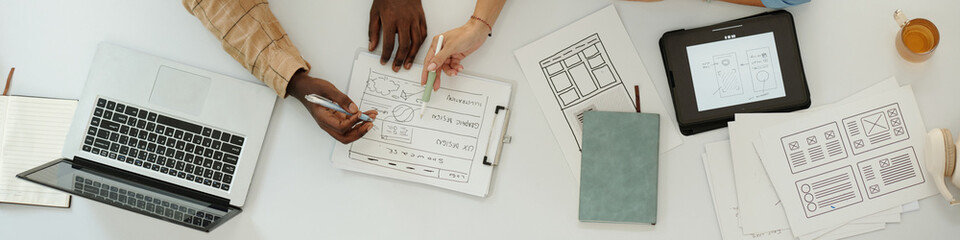 Diverse team collaborating on design sketches and plans, with laptop and tablet visible on table...