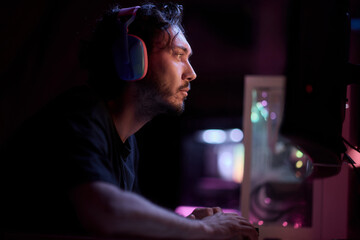 A devoted gamer sits in a vibrant neon lit room, completely engrossed in intense gameplay