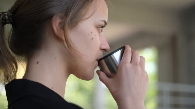 portrait of a young beautiful woman drinking herbal tea from a thermos on a warm spring day