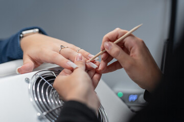 Professional manicurist girl doing manicure and trimming cuticle with wooden stick in beauty studio. Hand care