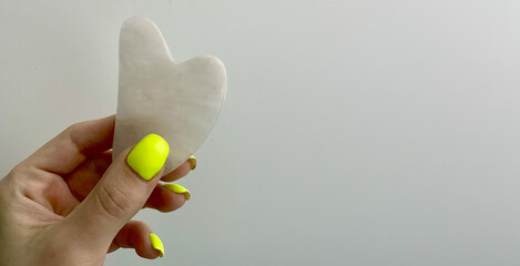 A female hand holding quartz gua sha face massager isolated white background