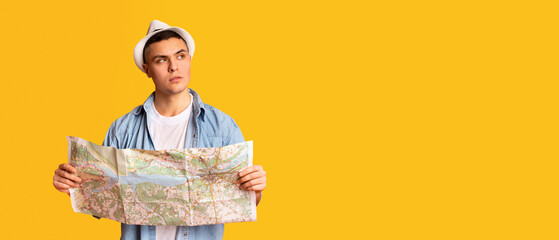Interested tourist handsome guy holding city map and looking at copy space, orange studio...