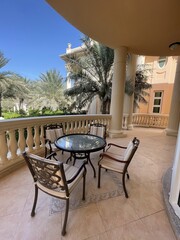 Elegant outdoor seating area with a glass table and four chairs in a sunny courtyard