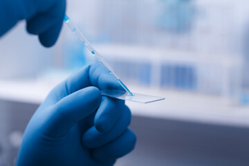 A scientist's hand in a glove holds a pipette and Microscope glass