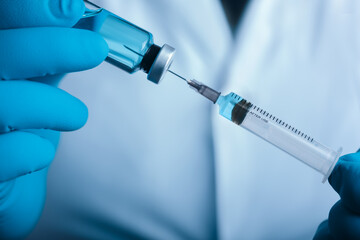 A blue-gloved medic's hand holds a syringe and test vaccine