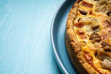 Quiche Laurent according to a traditional French recipe. Pie with chicken and mushrooms on a blue plate with a light blue napkin on a blue background. Place for text.