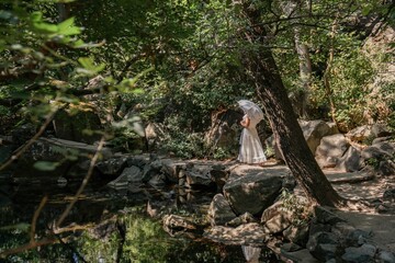 Woman, Forest, Waterfall - A woman wearing a white dress walks through a lush forest with a waterfall in the background.