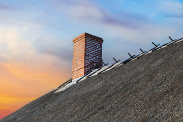 Brick chimney on a traditional thatched roof with a vibrant sunset sky in the background. Rustic...