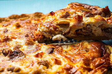 Quiche Laurent according to a traditional French recipe. Pie with chicken and mushrooms on a plate on a blue background. A piece of pie is cut with a knife.