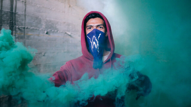 adult man wearing a blue face mask surrounded by green smoke