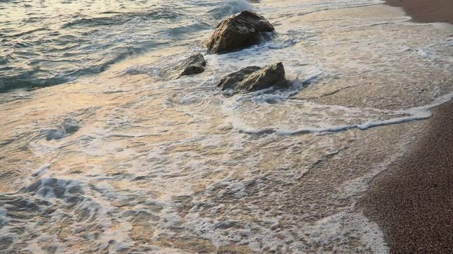 Waves gently lap at shore during stunning sunset over ocean. Golden sunlight reflects off waves as they roll onto shore, creating tranquil atmosphere at sunset by sea. Montenegro summer, Canj