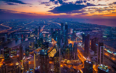 Fototapeta premium A vibrant city skyline of Dubai is illuminated as the sun sets, casting a warm glow over skyscrapers and the bustling streets below. The panoramic view showcases urban life in UAE.