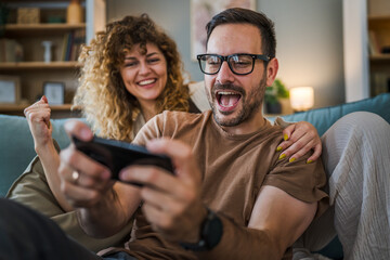 couple man and woman husband wife play smart phone video games at home