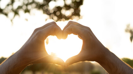 Obraz premium Hands in shape of love heart at sunset. The sun is setting in the background, creating a warm and romantic atmosphere. 