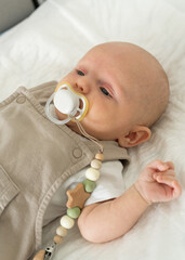 Newborn baby boy is lying on bed holding pacifier in his mouth. Child is trying to sleep.