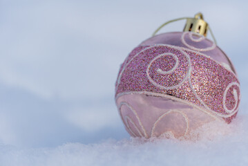 Pink shiny christmas toy ball lying on the white snow in winter. Christmas and new year holidays...