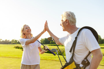 elderly senior couple in uniform celebrating victory and success in golf game and giving high five, old man and woman playing golf on golf course at sunset and doing outdoor sports