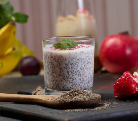 A glass with chia seeds and yogurt, pomegranate seeds are added to the dessert. A wooden spoon is...