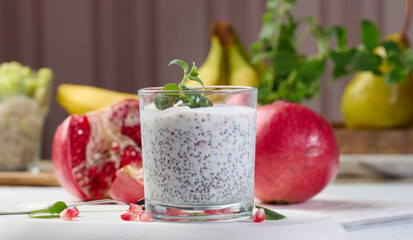 Glass with chia and yogurt dessert decorated with fresh fruits and pomegranate seeds on white table
