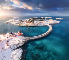 Aerial view of road and bridges, snowy islands with red rorbu, sea, water, mountains, cloudy sky at sunset in winter. Beautiful north landscape. Top view of Henningsvaer, Lofoten islands, Norway © den-belitsky